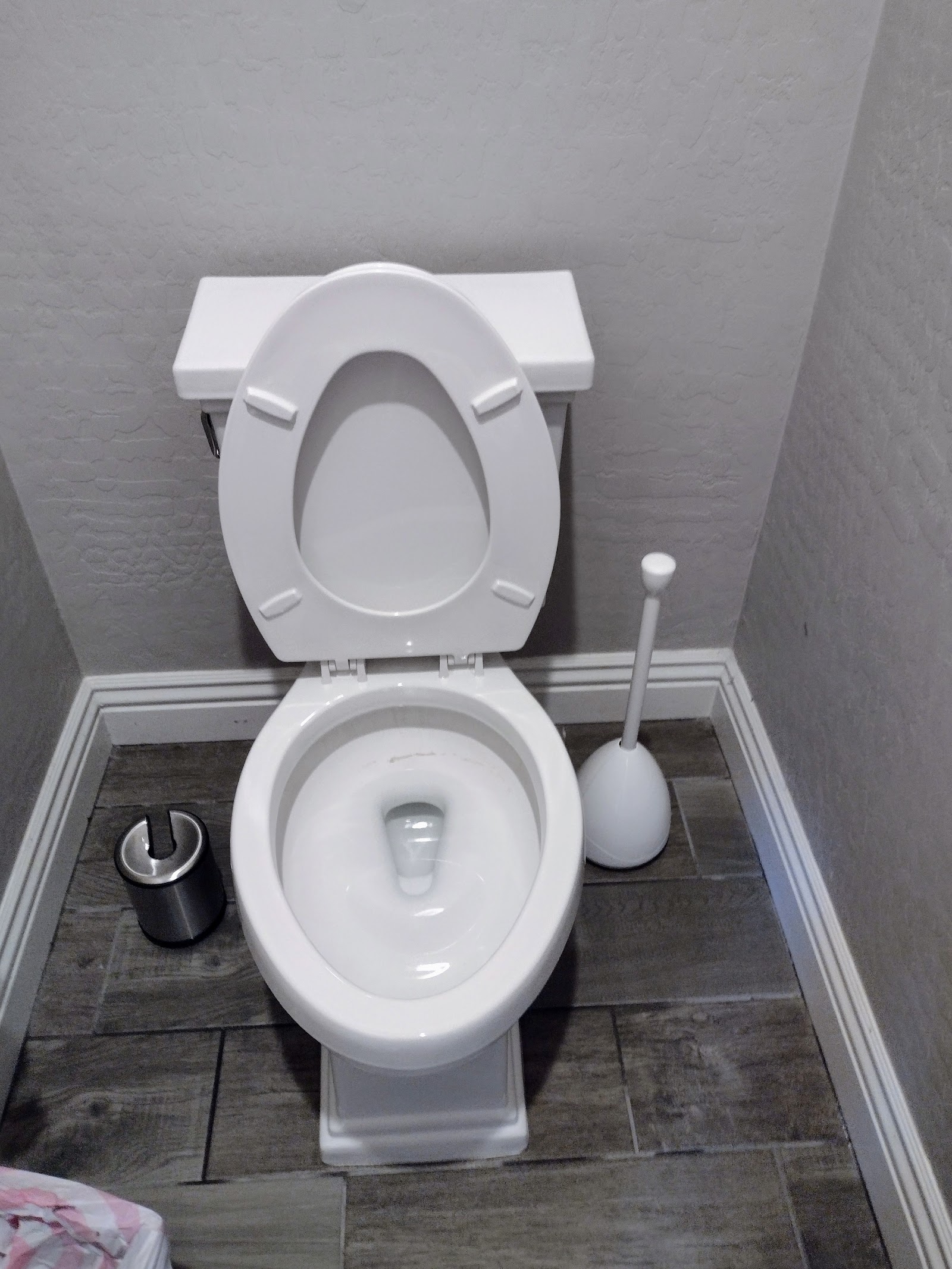 Clean white toilet with plunger and waste bin in bathroom corner